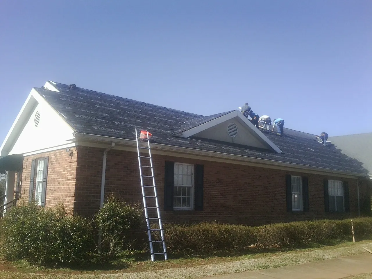 Crew tearing shingles off a brick ranch roof with a ladder set — Emergency Roof Repair work by our crew in Moorefield
