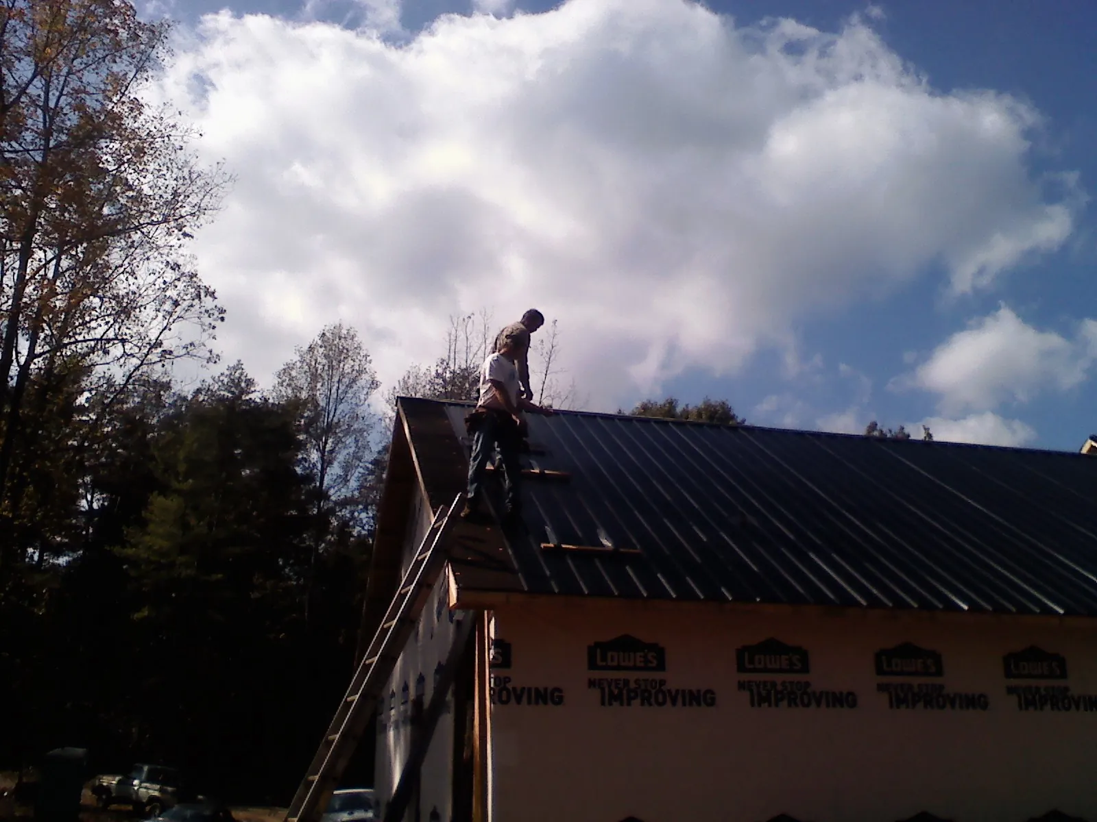 Roofer fastening dark metal panels high against a cloudy sky, from a Roof Inspection job in Moorefield